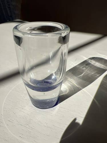 Reviewer's Shot Glass with Cremation Ash on a sunlit surface, highlighting the ash sealed within the thick glass base.