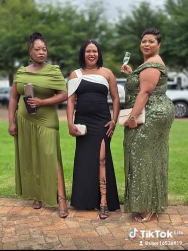 Reviewer smiling in the elegant black and white off-shoulder dress with a high slit, standing between two friends.