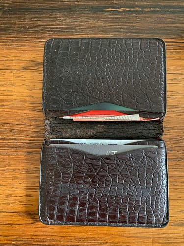 Customer's open, textured brown wallet on a wooden surface, showing card slots inside.