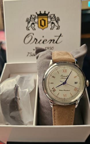 Cliente muestra el reloj Orient Bambino en su caja blanca de edición limitada, con correa de gamuza clara.