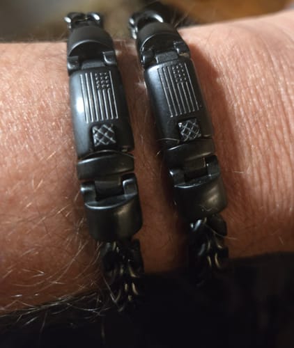 Close-up of a reviewer's wrist showing two black Black Mamba bracelets with their American flag clasps.