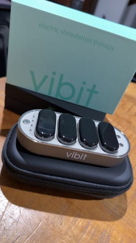 Customer's Vibit TENS device resting on its black case, with the product's light blue box visible in the background.