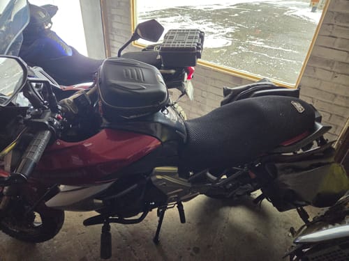 Customer's black Wind Rider Seat Cover installed on their red and black motorcycle parked indoors.