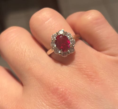 Customer's hand wearing the oval halo ruby ring, showing the vivid red stone and gold band.