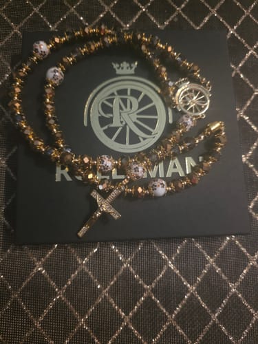 Klant toont de Ave Maria Nomads Rozenkrans met goudkleurige en witte kralen, liggend op de verpakking.