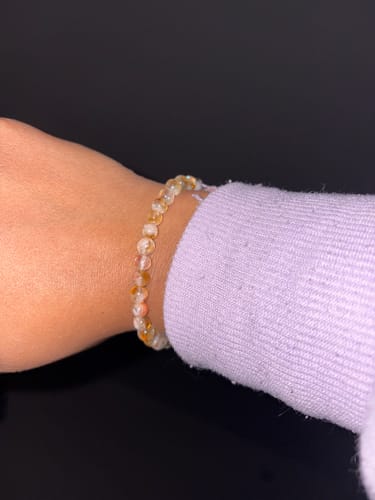 A customer wearing the beaded STACKER - CITRINE bracelet on their wrist next to a purple sleeve.