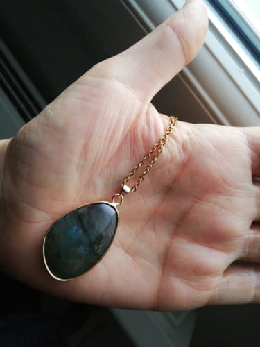 Client tenant le collier en Labradorite dans la paume de sa main, montrant les beaux reflets bleus de la pierre.