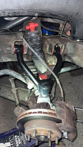 Customer's black Lift Upper Control Arm with red bushings installed on the front suspension of a truck.