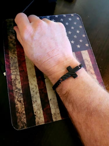 Customer wearing the black In God We Trust cross bracelet on their wrist, resting on an American flag mousepad.
