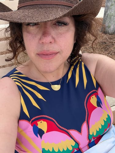 Reviewer wearing the gold Ellie® Sunburst Semicircle Necklace with a colorful top while sitting outside.