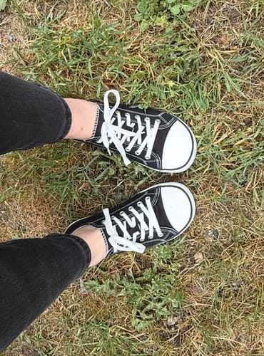 Reviewer standing on grass, wearing the classic black Roam I - Barefoot Shoes with white laces.