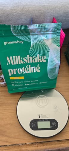 Le sachet vert de Milkshake protéiné d'un client, posé sur une table à côté d'une balance de cuisine numérique.