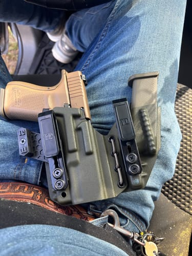 Customer's dark AXIS ELITE holster holding a tan handgun and spare magazine, resting on their lap.