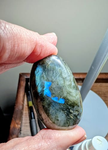 Customer's hand holding a polished Labradorite Moonstone item with a bright blue iridescent flash.