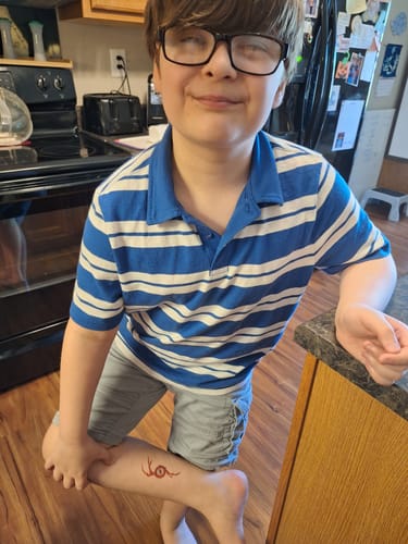 A customer's child smiling and showing the Eyeder SKETCH temporary tattoo on their leg.