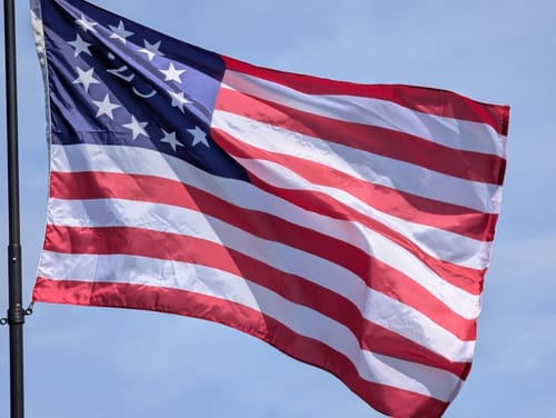 Reviewer's America 250 Betsy Ross Flag waving on a flagpole against a bright blue sky.