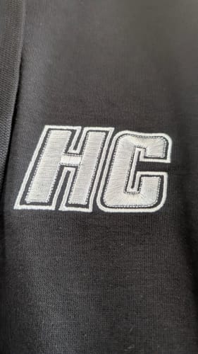 Gros plan d'un client sur la broderie argentée 'HC' du sweat à capuche noir Hoodie HC Argenté.