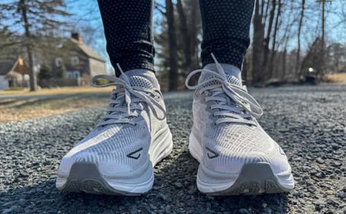 Reviewer wearing gray Ortho Walk shoes, standing on a gravel path outdoors.