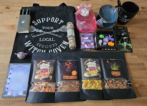 Rezensent zeigt den vielfältigen Inhalt der Witchy Box, darunter eine Tasche, Teesorten und eine Tasse.
