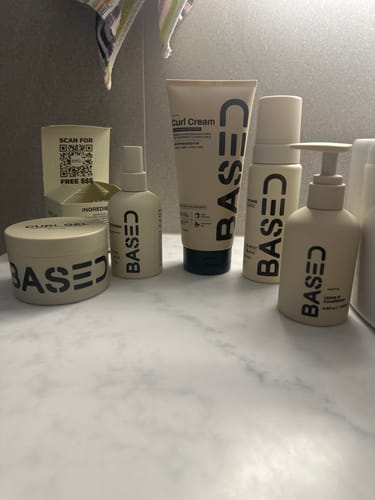 Customer's Based Curl Cream tube shown with other products from the same line on a bathroom counter.