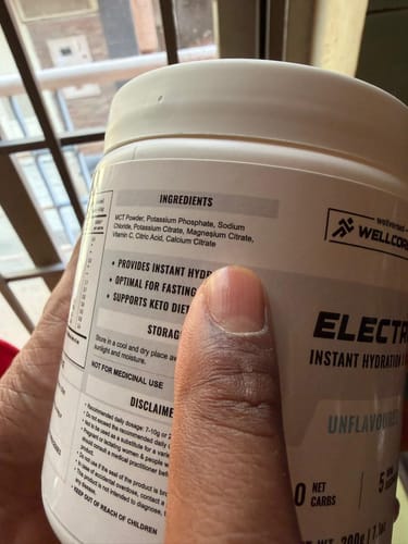 Customer holding the Wellcore Unflavoured Electrolytes tub, showing a close-up of the ingredients list.