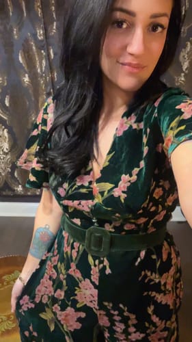 Reviewer wearing the green floral velvet jumpsuit, styled with a wide belt to show the fit.