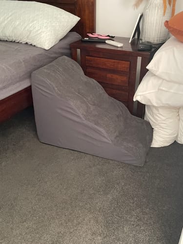 Customer's grey Soft Foam Dog Stairs placed on the floor next to a bed.