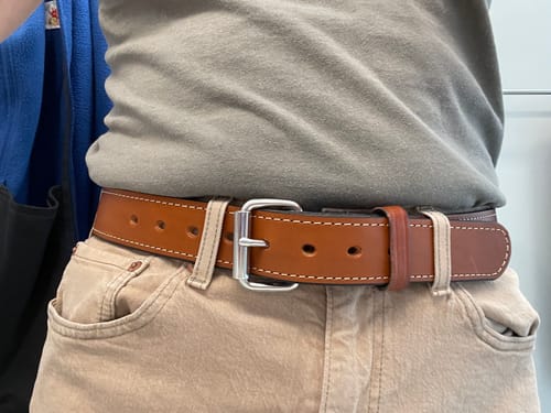 Reviewer's close-up of the brown Gunner Stitched belt, showing the steel buckle and stitching detail on khaki pants.
