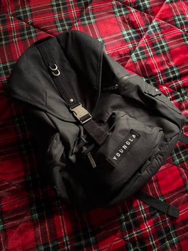 Customer's black Tactical Backpack lying on a red plaid blanket, showing the front buckle and multiple pockets.