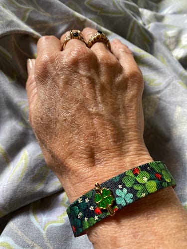 A reviewer's wrist wearing a patterned fabric bracelet featuring the gold and green Lucky Charm.