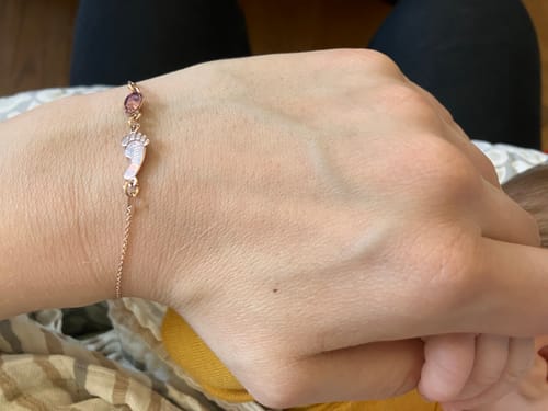 Kundin trägt das roségoldfarbene Armband "Babyfuß" mit Geburtsstein am Handgelenk und hält dabei eine Babyhand.
