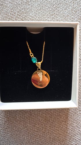 Kunde zeigt die goldene Geburtsstein-Halskette mit einem gravierten Fußabdruck-Anhänger und einem türkisfarbenen Stein in ihrer Box.