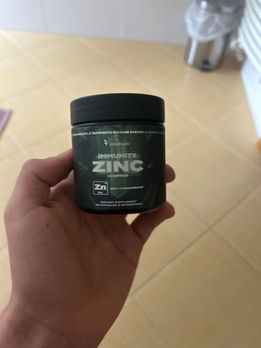 Reviewer holding the dark green tub of Immunity Zinc in their hand against a tiled counter.