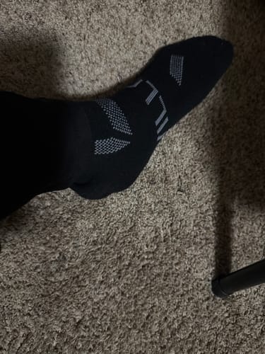 Reviewer's foot in a black Men's Alpaca Sock, showing the ankle height and grey pattern.