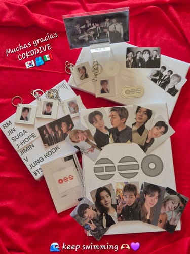 Reviewer displays the contents of the BTS ARIRANG album set, including photocards and keyrings, arranged on a red surface.