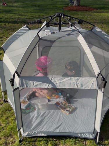 Customer's gray Pop 'N Go® LUXE Playpen set up on grass with two children playing inside.
