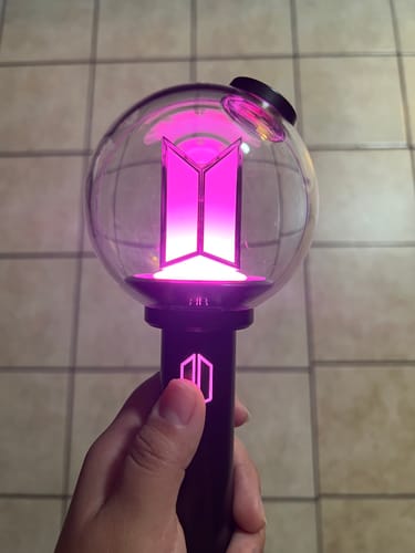 Customer holding the BTS Official Light Stick Ver.4, which is illuminated with a vibrant purple light.