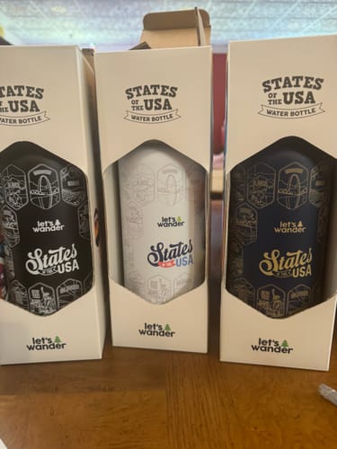 Reviewer's three Lets Wander™ water bottles in black, white, and navy, displayed side-by-side in their packaging.