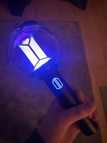 Customer holding the BTS Official Light Stick Ver.4, which is glowing with a vibrant blue light in a dark room.