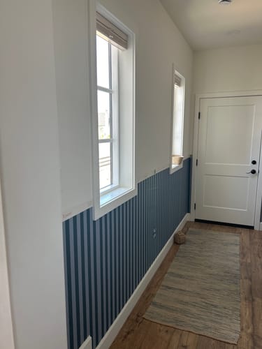 Customer's Hayes Wallpaper with blue vertical stripes applied to the lower half of a white hallway wall.