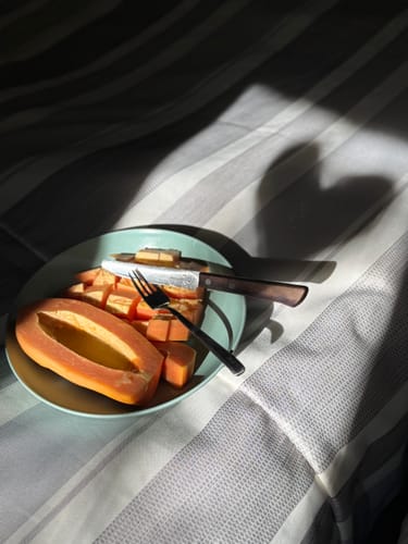 Ein Kunde zeigt eine aufgeschnittene und gewürfelte Bio-Papaya auf einem Teller, die in der Sonne liegt.