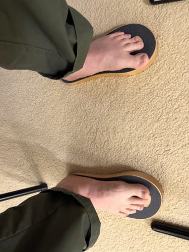 Customer's feet, viewed from above, standing on two black SoleSteps® platforms on a carpet.