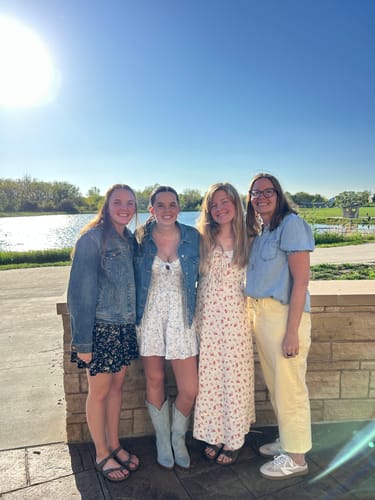 Reviewer (on right) wearing the Easygoing Chambray Blouse with yellow pants, standing with friends outdoors by a lake.