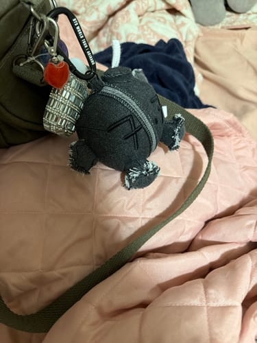 Customer's BTS ARMY BOMB PLUSH KEYRING in dark fabric, clipped onto a bag strap.