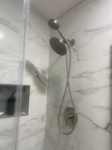 Reviewer's brushed nickel dual shower head system installed in a new marble-tiled shower.