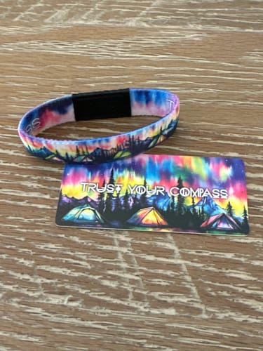 Customer's Trust Your Compass Bracelet and matching collector's card with an aurora design on a wooden surface.