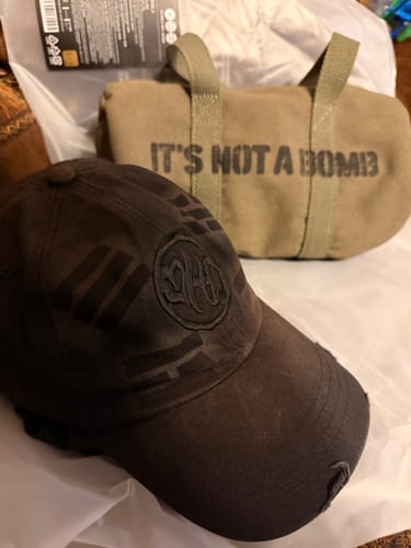 Customer's official BTS light stick bag, a tan canvas bag with the words "IT'S NOT A BOMB" printed on the side, next to a baseball cap.