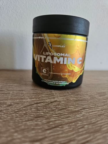 Reviewer's black tub of Liposomal Vitamin C with a yellow label sitting on a wooden surface.