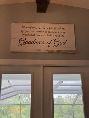 Customer's Goodness of God Faith Sign hanging on a gray wall above a set of double doors.
