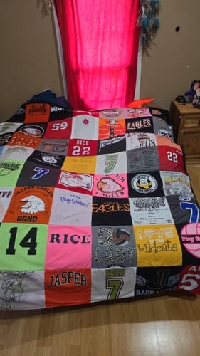 Customer's colorful Project Repat T-Shirt Quilt made of sports and school shirts, spread out on a bed.
